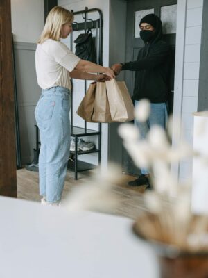 A woman receives a delivery package from a courier at her doorstep inside a modern home.