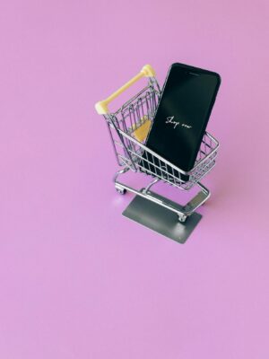 Mobile phone in mini cart on pink surface, symbolizing online shopping.